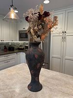 Tall Raku vase with dried rose and leaf arrangement on kitchen countertop, showing front view.