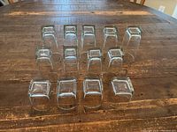 Top-down view of the 13 clear glass tumblers arranged on wooden table showing varying sizes and square bases.