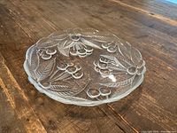 Top view of clear thick glass platter showing grape clusters and leaf etching with scalloped edges, sitting on wooden surface.