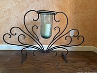 Front view of large wrought iron decorative candle holder with scrollwork fan design and central blown glass holder containing a white candle.
