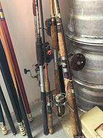 Group of eight fishing rods leaning against wall, some with reels attached