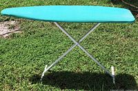 Side view of turquoise-covered foldable ironing board on grass