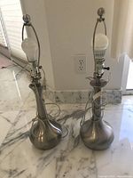 Both silver-tone table lamps standing side by side showing bases, harps, bulbs and cords