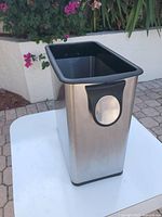 Rectangular stainless steel waste basket with black plastic rim and base placed on table