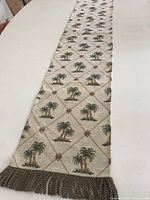 Full view of beige side of reversible palm tree patterned table runner with fringe