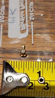 Front view of the small 14K gold pendant placed next to a tape measure showing size under 1 cm.