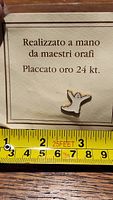 Ghost pin attached to card with Italian text stating it is handmade by master goldsmiths and plated with 24 kt gold, measuring about 2.5 cm wide.