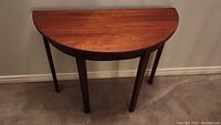 Full view of antique wooden half moon table against a wall, showing its shape and wood grain.