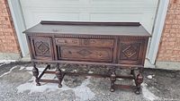 Full view of antique oak sideboard showing carved doors and drawers, turned legs, and overall design.