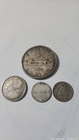 Overall lot showing four Canadian coins including the 1963 silver dollar and smaller coins