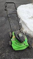 Full view of used green Lawn-Boy push lawn mower with black engine housing on driveway next to snow.