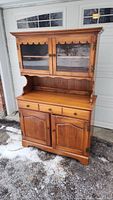 Front view of maple hutch outdoors showing full piece with upper glass doors and lower wood cabinet doors.