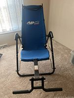 Blue Ab Lounge Sport ab exercise machine with padded seat and backrest and tubular black metal frame, placed indoors on carpet.