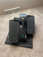 Front view of the Cubii elliptical with foot pedals, resistance knob, digital display, and mat underneath on carpet.