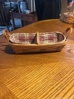 Longaberger basket showing full side profile with handles and plaid fabric liner, sitting on wood table.