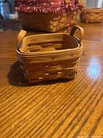 Small rectangular woven wood basket shown standing on wooden table with two upright handles visible