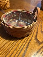 Side angled view of the small woven basket showing leather strap handles and the plaid fabric liner inside, with a transparent divided insert.