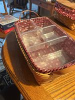 Photo of rectangular wooden Longaberger basket filled with transparent plastic divider and red fabric liner with white snowflake pattern, on a round table.