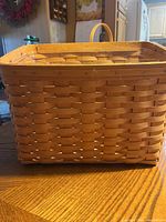 Front view of rectangular woven basket with wooden handles on a wooden surface.