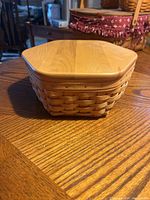 Hexagonal Longaberger basket with a wooden lid on a wooden table.