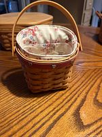 Front view of the Longaberger basket showing the woven wood, handle, and fabric liner with heart-shaped buttons on the liner attachment.