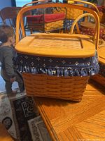 Side view of woven basket with wooden lid and blue fabric liner showing floral pattern and decorative trim.