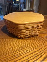 Closed view of hexagonal woven basket with smooth wooden lid on top, resting on wooden table.