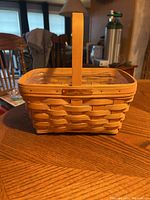 Front view of rectangular woven Longaberger basket with single wooden handle and metal plaque