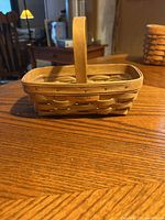 Front view of the rectangular woven wooden basket with handle sitting on wooden table.
