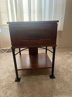 Front view of wooden nightstand showing single drawer with metal handle, lower shelf, and black metal legs.