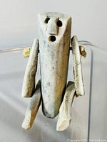 Front view showing carved human face and body, arms and legs attached with rope.