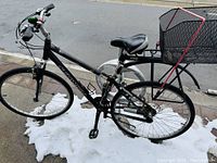 Side view of the full bicycle showing black aluminum frame, tires, pedals, seat, and attached rear basket with bungee cords.