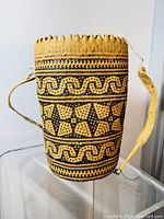 Front view of a cylindrical, handwoven rattan backpack with natural and black tribal pattern designs and woven strap.