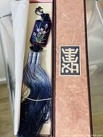 Traditional Korean silk norigate tassel in its decorative box, showing the full length and floral embroidery on the pendant with attached long silk tassels.