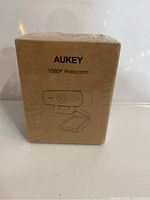 Front view of the Aukey 1080P Webcam packaging in brown box sealed with plastic.
