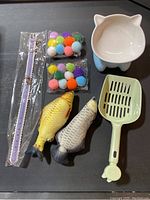 Full set of cat essentials including cat shaped bowl, fish toys, pom-pom balls, bell collar, and litter scoop