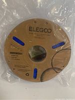 Photo of a sealed spool of blue Elegoo 3D printer filament on a brown cardboard reel, label showing 1.75mm diameter, 1KG weight.
