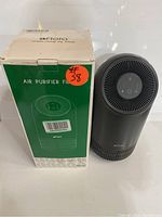 Floia air purifier next to its original boxed packaging showing front of the box and product shape.