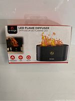 Front view of diffuser box showing LED flame diffuser image, brand e-mrge, and icons for simulated flame, quiet operation, and auto off.