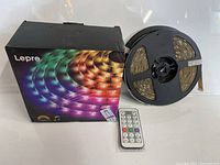 Lepro LED strip light spool, remote control, and packaging box arranged on a white background showing the items included in the lot