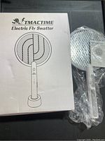 Photo showing one TMACTIME Electric Fly Swatter outside of packaging with plastic wrap and manual, next to the product box.