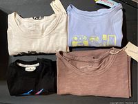 Four folded T-shirts seen from front showing various colors and graphics