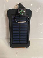 Front view of solar power bank showing solar panel, compass on strap, and carabiner attached.