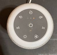 Top view of white noise machine showing round control panel with touch buttons and indicator lights.