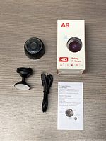 The entire lot contents including the IP camera, mounting stand, USB charging cable, user manual, and original product box showing brand A9 and features.