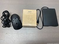 Bundle of AUKEY 1080P webcam in sealed box, black USB floppy drive, and black wired USB mouse on wood surface.