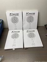 Four boxed TMACTIME Electric Fly Swatters, stacked two by two, boxes white with black line drawings of the swatter on the front.