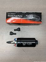 Black Evil Energy electric fuel pump with terminals and connectors shown from side angle on light surface.