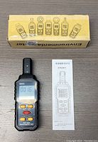 Overall view of the S8602 EMF tester, user manual, and original box laid out on table.