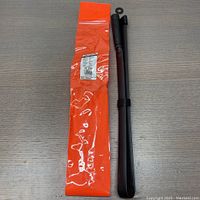 Full view of folded black foldable antenna next to orange storage pouch on grey surface.